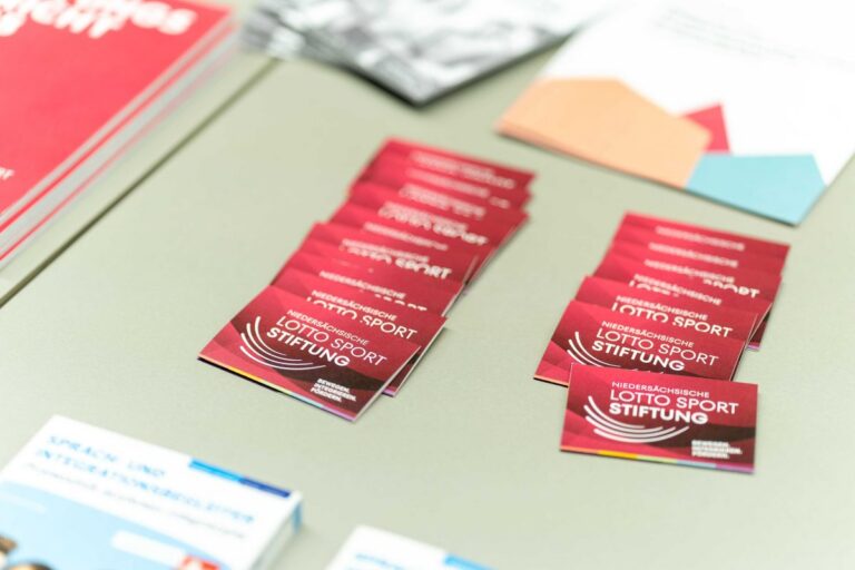Rote Karten mit dem Logo der Niedersächsischen Lotto-Sport-Stiftung liegen neben Broschüren auf einem Tisch.