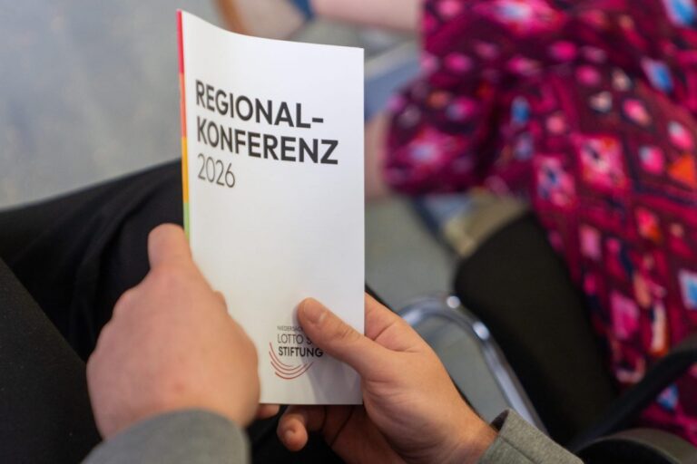 Eine Person hält eine Broschüre mit der Aufschrift „Regionalkonferenz 2026“ in beiden Händen.