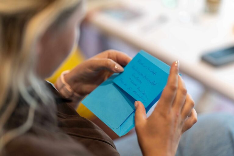 Eine Person hält blaue Moderationskarten mit handschriftlichen Notizen und einen Stift in den Händen.