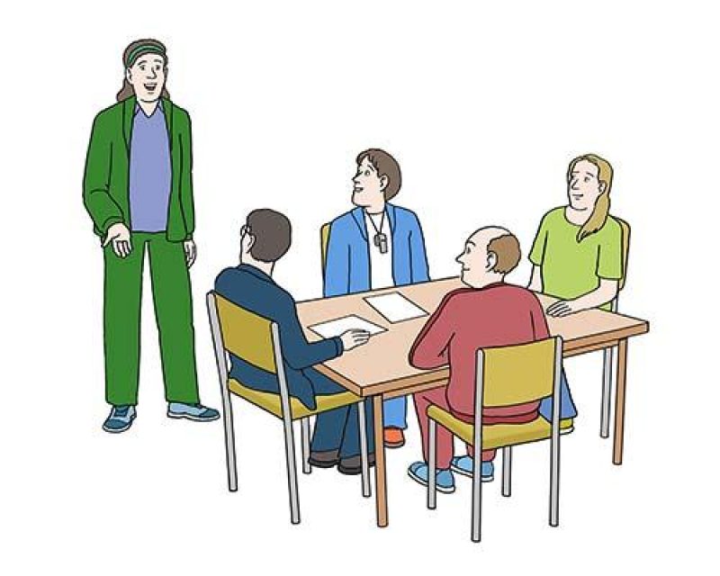 Vier Personen sitzen an einem Tisch, eine fünfte steht daneben und spricht.