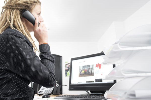 Mitarbeiterin telefoniert am Schreibtisch vor einem Bildschirm.