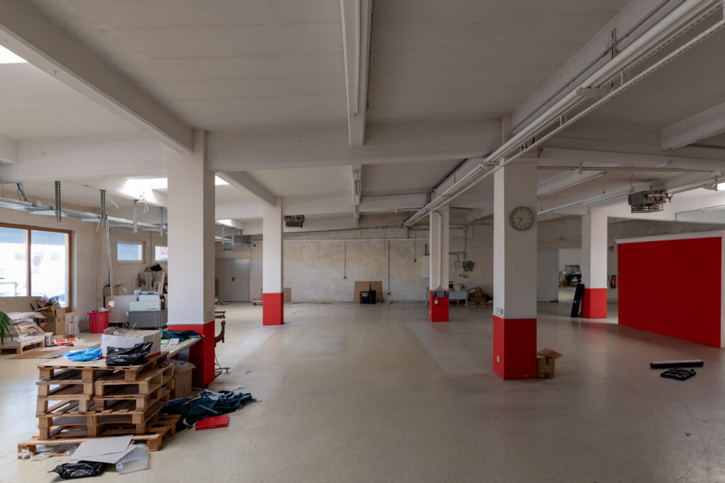 Große Halle mit Stützpfeilern, rot gestrichenen Pfeilerfüßen und gelagerten Paletten.